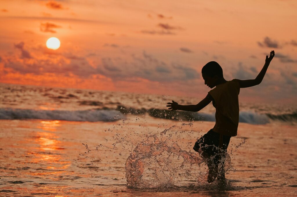 A child joyfully splashing in the ocean waves during a vibrant sunset, capturing pure happiness and freedom.