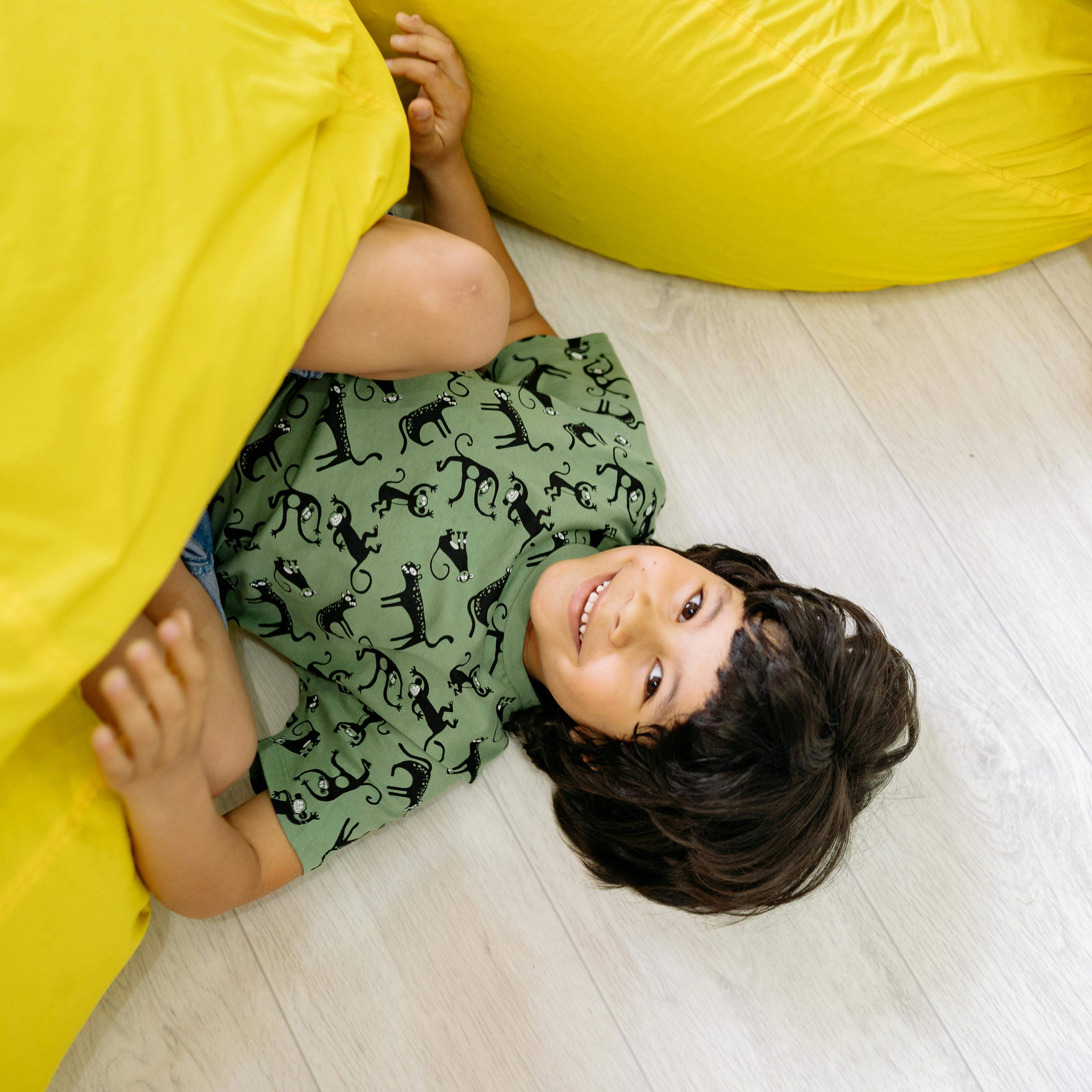 A smiling child lying between yellow bean bags indoors, exuding joy and happiness.